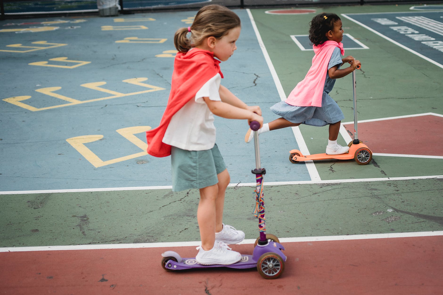 girls with capes racing with kick scooters in the playground